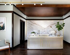 Reception desk with marble backdrop, wood accents, and minimalist decor in a modern lobby setting at The Ambrose Hotel Santa Monica.