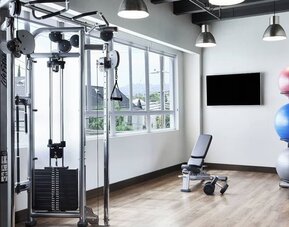 Fitness center with weight machine, bench, exercise balls, and large windows letting in natural light at AC Hotel By Marriott Beverly Hills.
