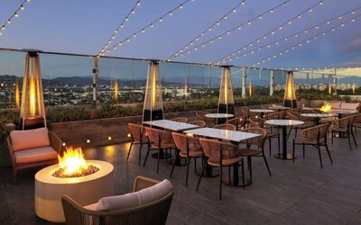 Rooftop terrace with seating, fire pits, string lights, and city skyline views at dusk at AC Hotel By Marriott Beverly Hills.