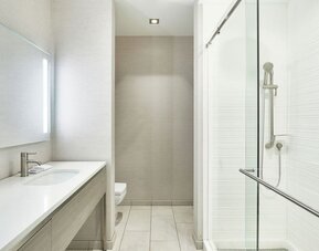 Modern bathroom with long vanity, illuminated mirror, glass shower enclosure, and neutral tile finishes at AC Hotel By Marriott Beverly Hills.