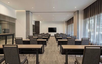 Meeting room with rows of tables and chairs, presentation screen, and large windows with curtains at AC Hotel By Marriott Beverly Hills.