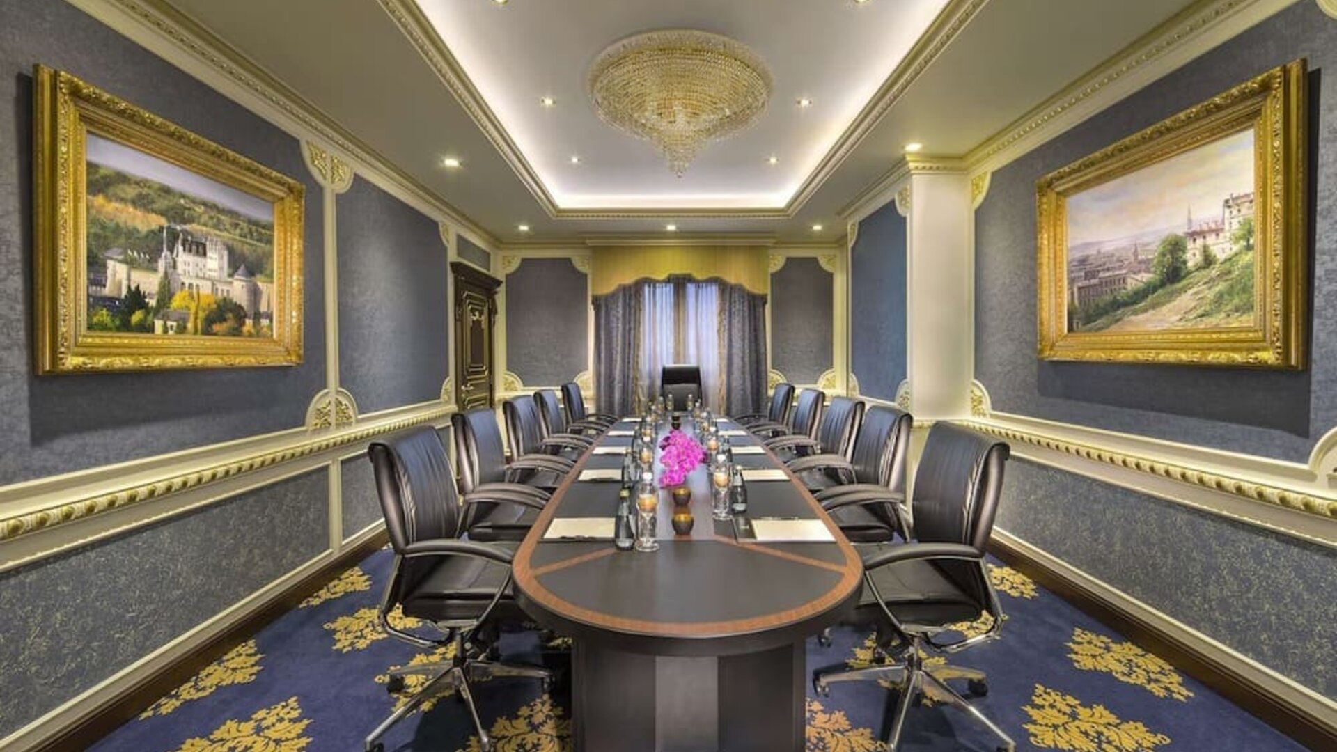 Long conference room with central table, leather chairs, chandeliers, and framed artwork