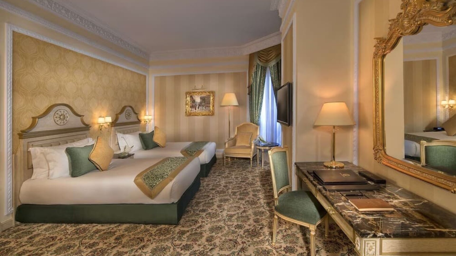 Twin bedroom with two beds, patterned carpet, armchair seating, and wall-mounted television