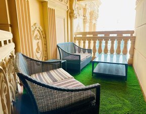 Narrow balcony with two wicker armchairs and a glass table on green turf, framed by ornate cream railings