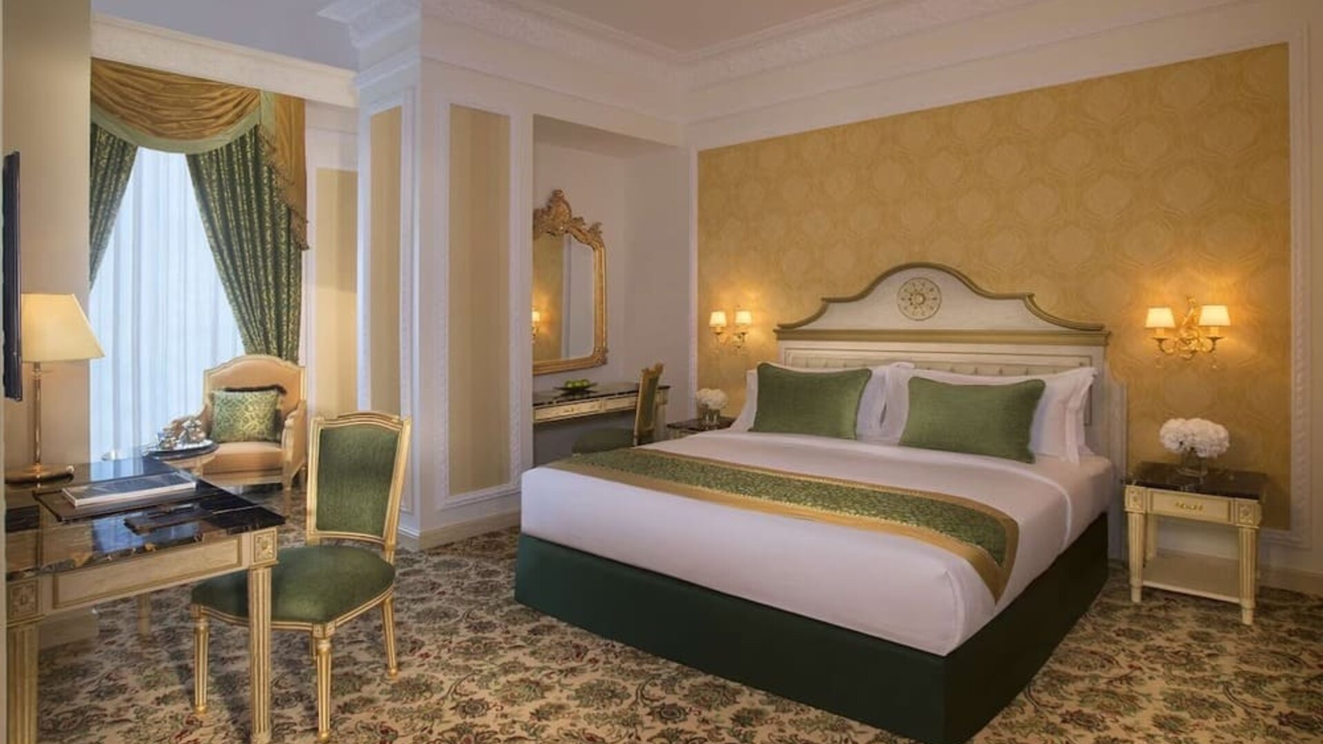 Elegant king bedroom with green accents, writing desk, and armchair seating near tall curtained window