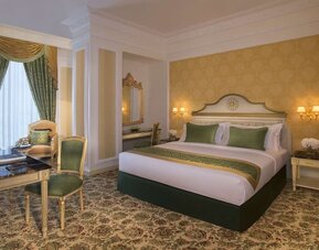 Elegant king bedroom with green accents, writing desk, and armchair seating near tall curtained window