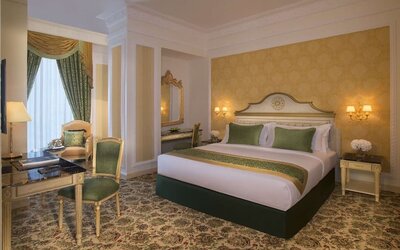 Elegant king bedroom with green accents, writing desk, and armchair seating near tall curtained window