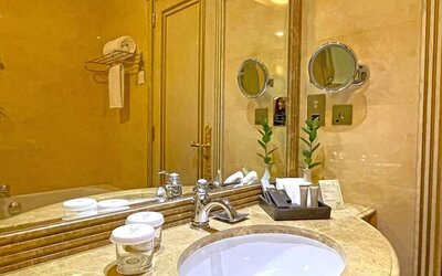 Marble bathroom vanity with round sink, large mirror, toiletries tray, and warm gold-toned finishes