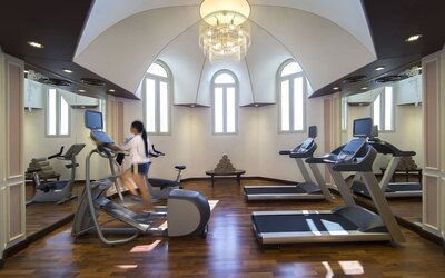 Bright fitness room with treadmills, elliptical machines, mirrored walls, and arched windows overhead