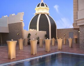 Rooftop terrace with small cocktail tables, domed structure, and reflecting pool under clear sky
