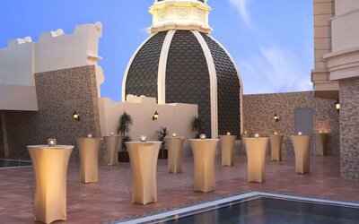 Rooftop terrace with small cocktail tables, domed structure, and reflecting pool under clear sky
