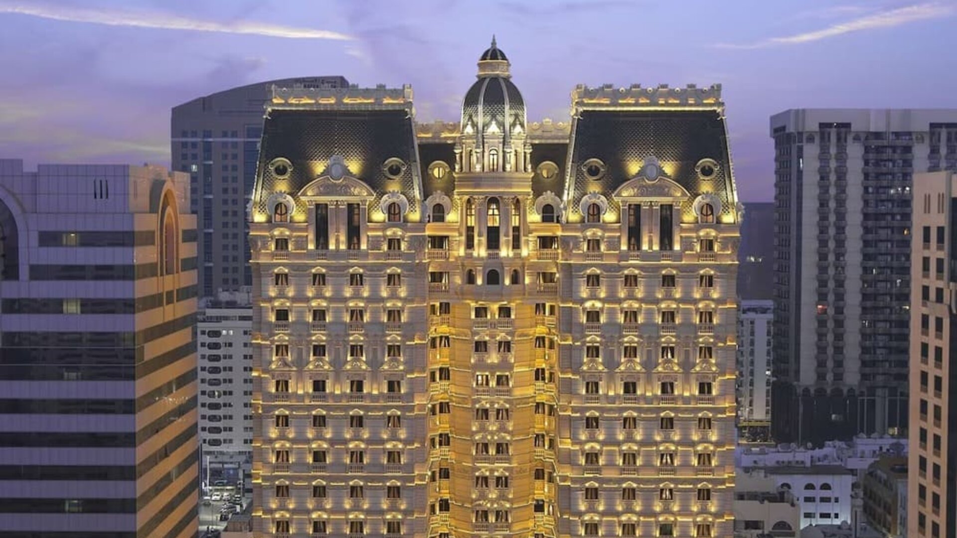 Illuminated multi-story hotel exterior at dusk with ornate façade and surrounding city buildings