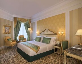 Classic king room with patterned carpet, armchair seating area, and desk beneath large mirror