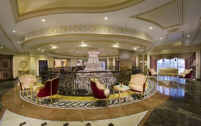 Upper-level lounge with curved railing, chandelier, and clusters of upholstered chairs and tables