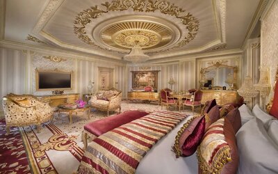 Luxurious suite with red and gold decor, ornate furniture, chandelier, and large bed