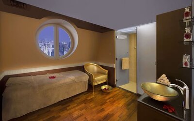Spa treatment room with massage bed, round window, glass shower, and wooden flooring