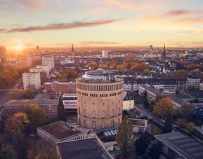 Aerial city view at sunset with round tower building centered among residential blocks and tree-lined streets