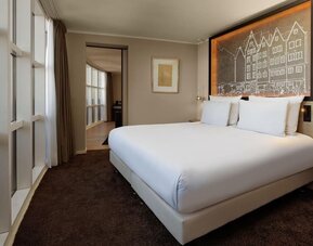 King room with large bed, decorative headboard, and wide window with city-facing view