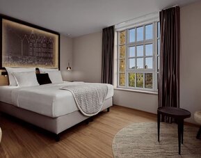 King room with lit headboard art, round rug, side table, and soft neutral tones throughout