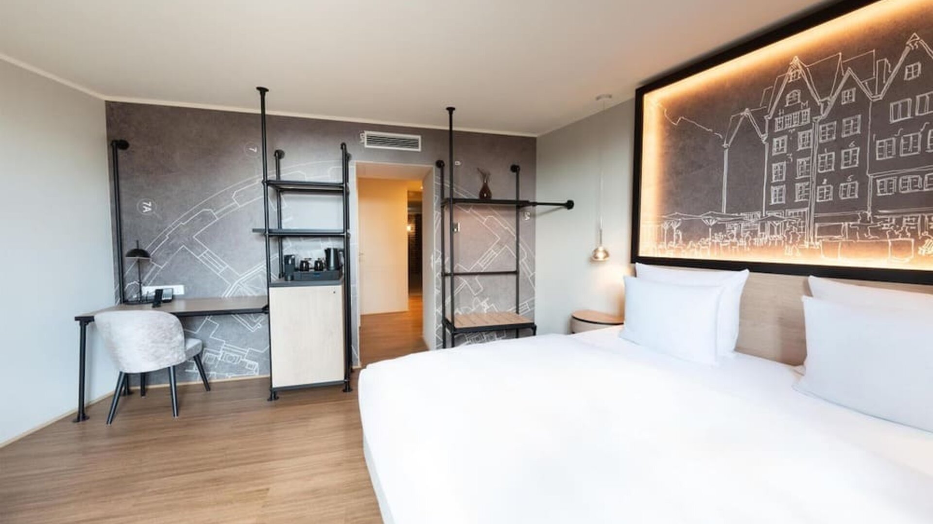King bed with white linens, wall art headboard, and narrow windowed corridor leading to separate seating area