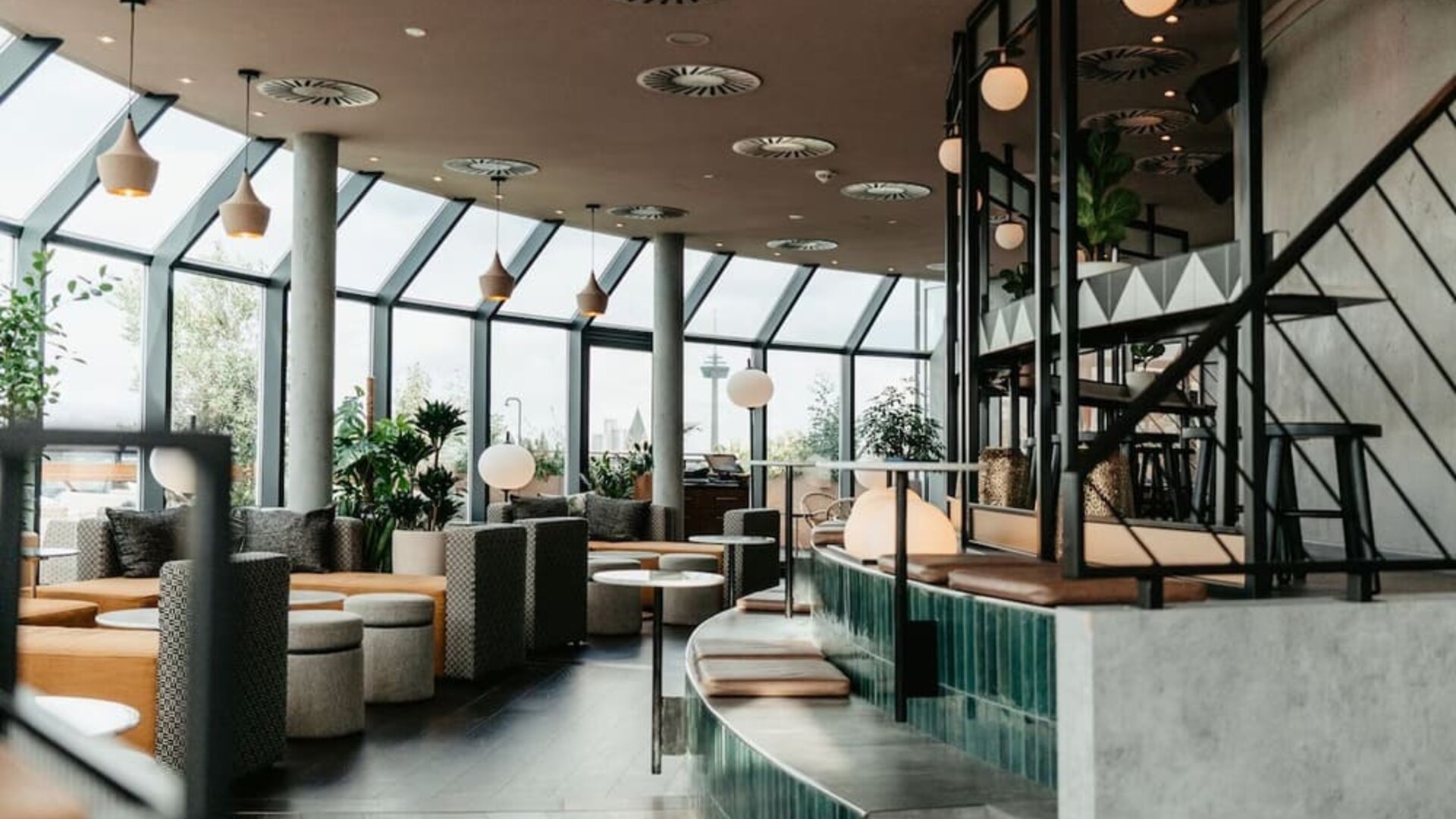 Restaurant space with floor-to-ceiling windows, bar counter, hanging lights, and casual seating areas