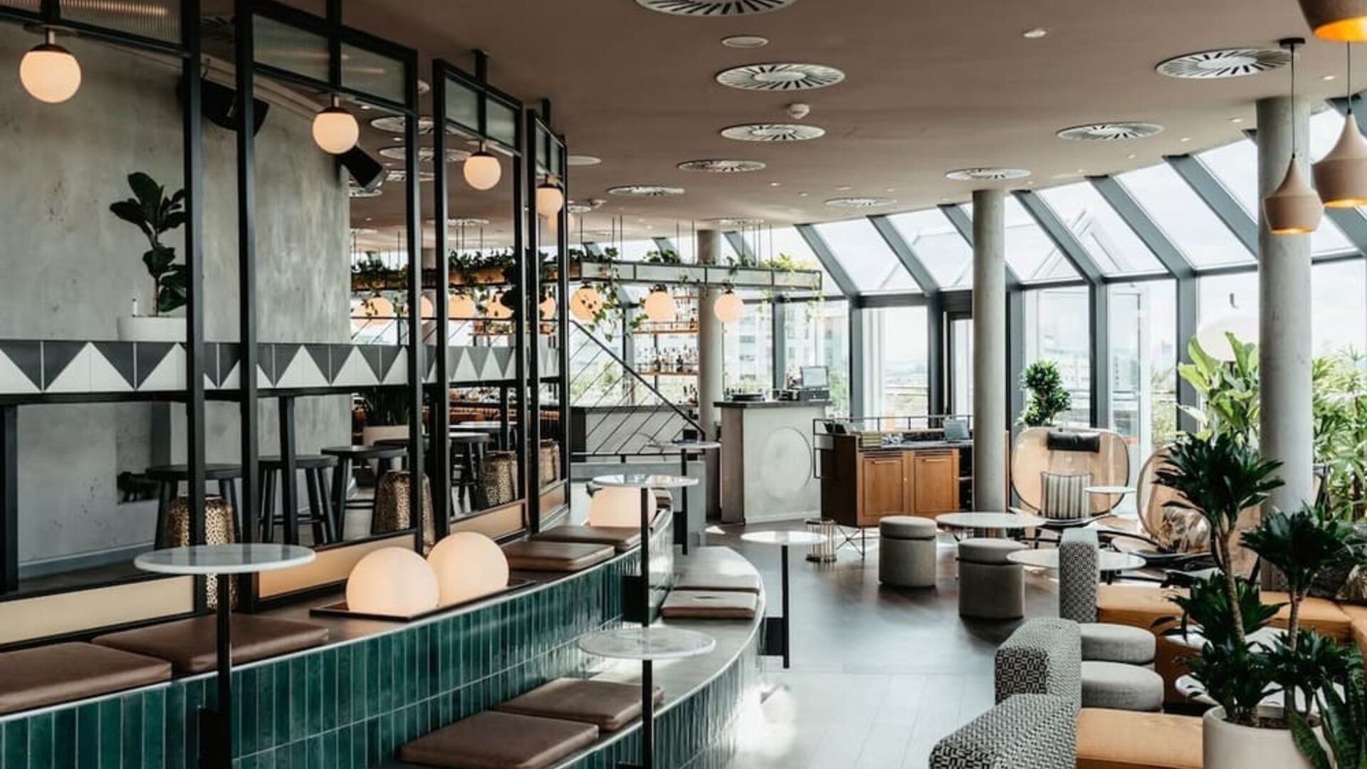 Open dining area with modern seating, greenery, bar section, and slanted glass ceiling allowing daylight