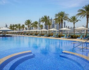 Outdoor pool with curved steps, palm trees, and rows of loungers and umbrellas along the deck