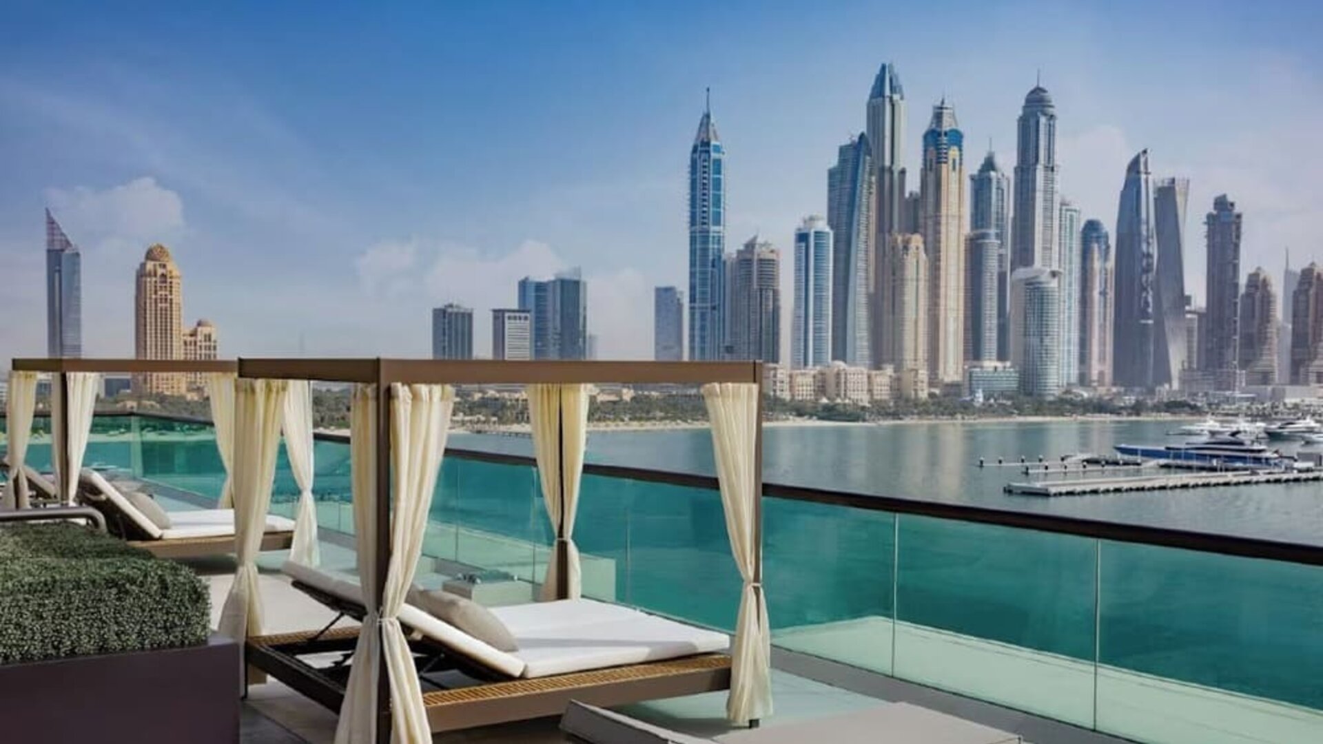 Private cabanas with cushioned loungers on terrace overlooking calm water and modern skyline