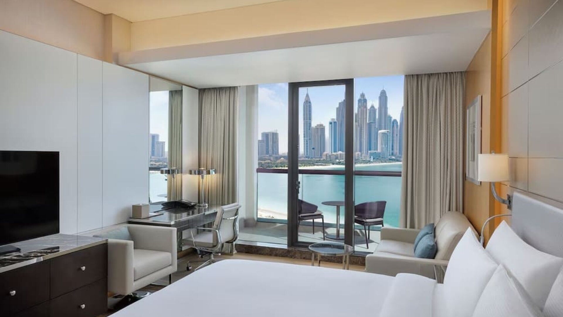 King bedroom with large bed, decorative headboard, desk area, and balcony with marina skyline view