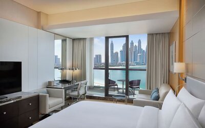 King bedroom with large bed, decorative headboard, desk area, and balcony with marina skyline view