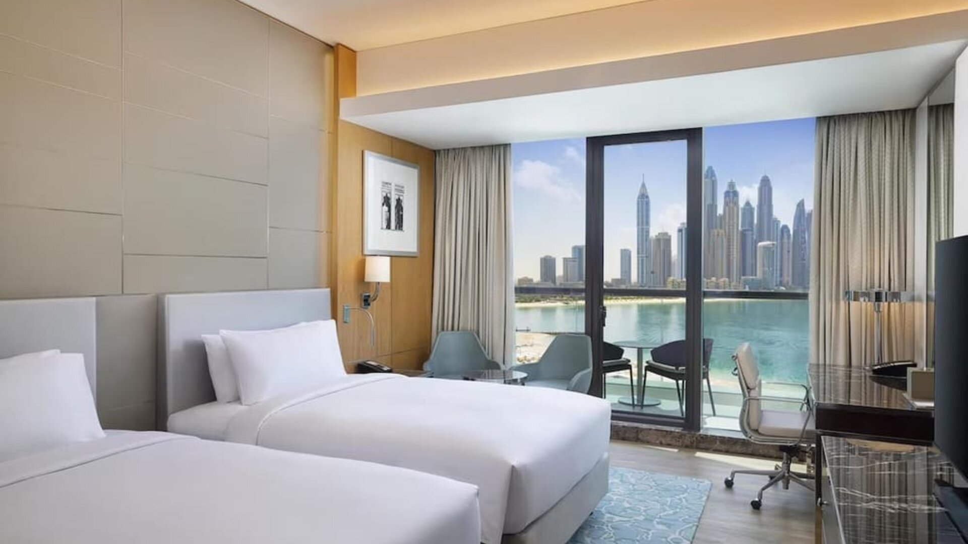 Twin bed guest room with floor-to-ceiling window, balcony seating, and waterfront skyline view