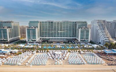 Beachfront hotel exterior with large pool, rows of loungers, and multi-story buildings facing the sea