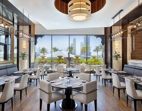 Restaurant dining room with upholstered chairs, pendant lights, and floor-to-ceiling windows to terrace