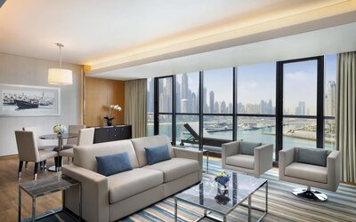 Living area with sofa, armchairs, dining table, and wide windows showcasing marina and skyline views