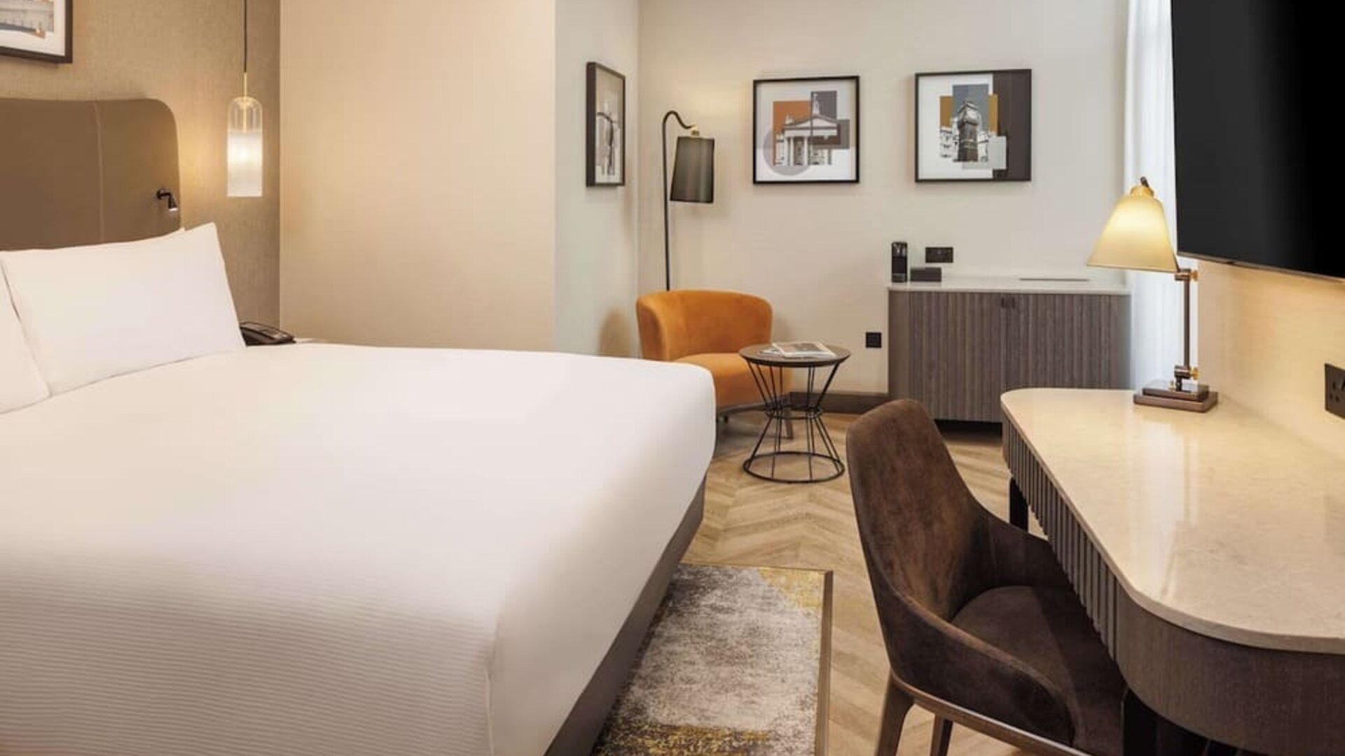 Modern king room with curved desk, leather chair, orange accent seating, and framed wall art