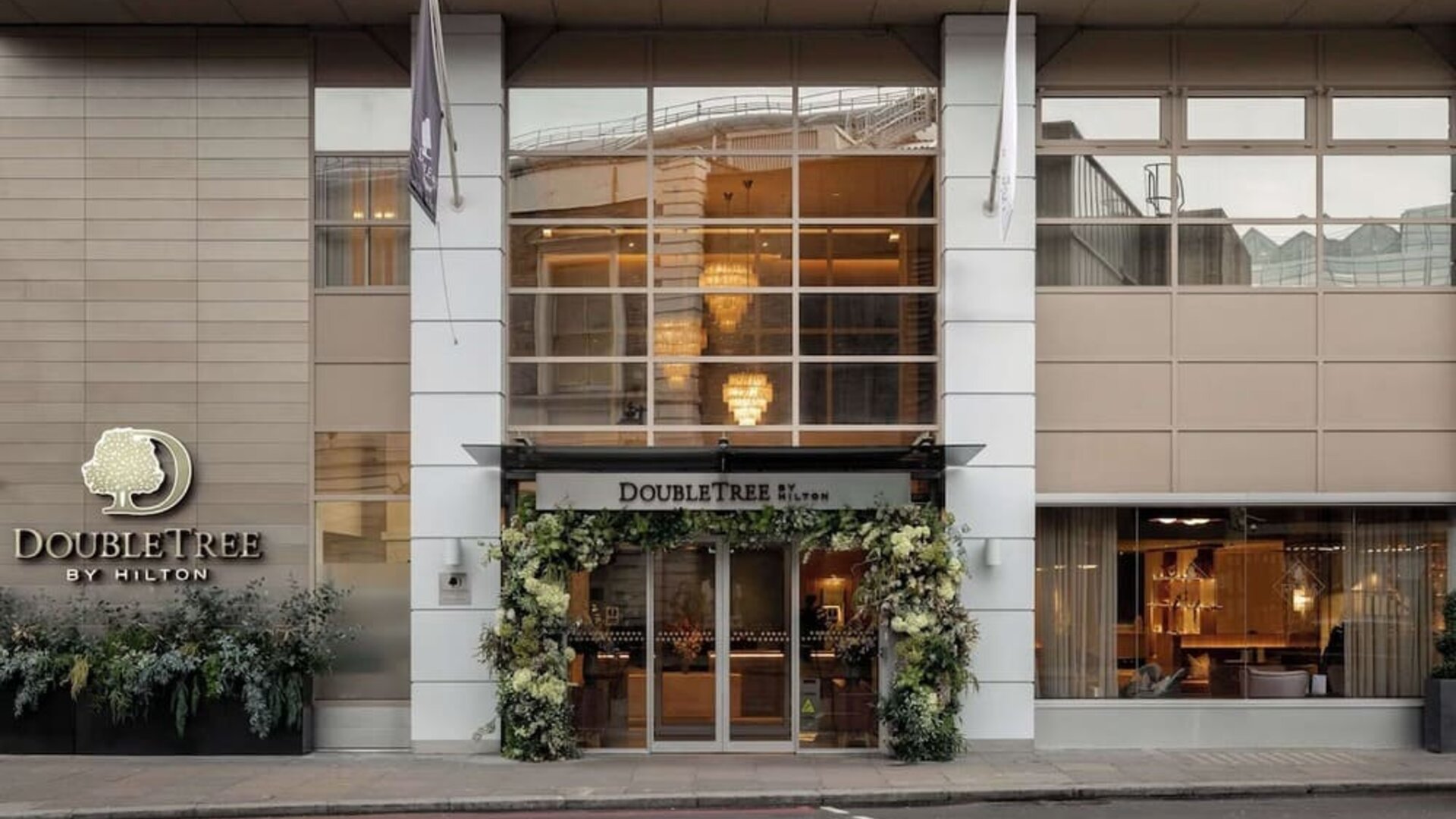 Street view of DoubleTree by Hilton entrance with large windows and floral decorations around doors