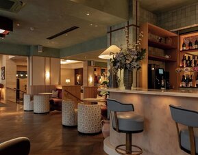 Hotel bar lounge with marble counter, upholstered stools, floral centerpiece, and warm lighting
