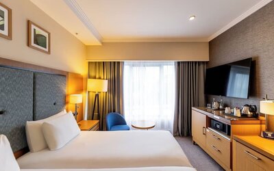 Bright guest room with king bed, oversized TV, blue lounge chair, and wood storage cabinets