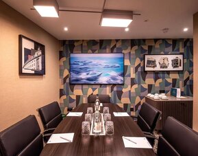 Private meeting room with long conference table, leather chairs, and wall-mounted television