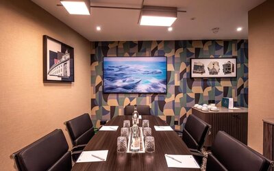 Private meeting room with long conference table, leather chairs, and wall-mounted television