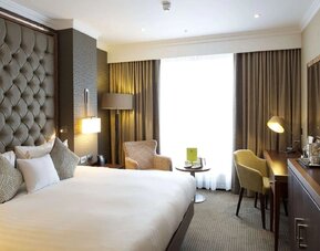 King bedroom with tall tufted headboard, armchair seating area, and desk beside bright window