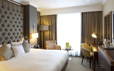 King bedroom with tall tufted headboard, armchair seating area, and desk beside bright window
