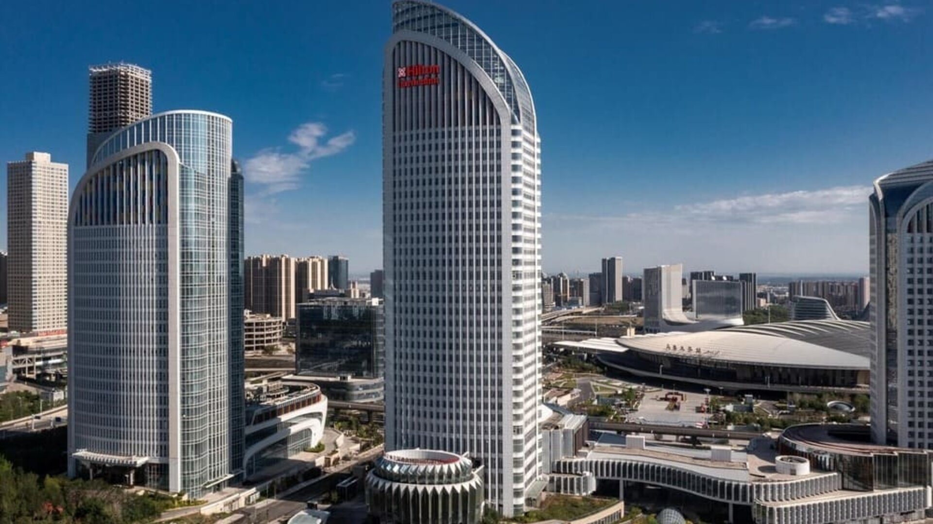 Curved glass high-rise towers beside a large convention center under a clear blue daytime sky