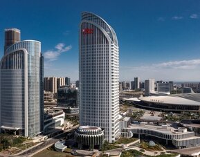Curved glass high-rise towers beside a large convention center under a clear blue daytime sky