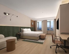 Spacious king room with green upholstered headboard, sofa seating, desk, and large city-view windows
