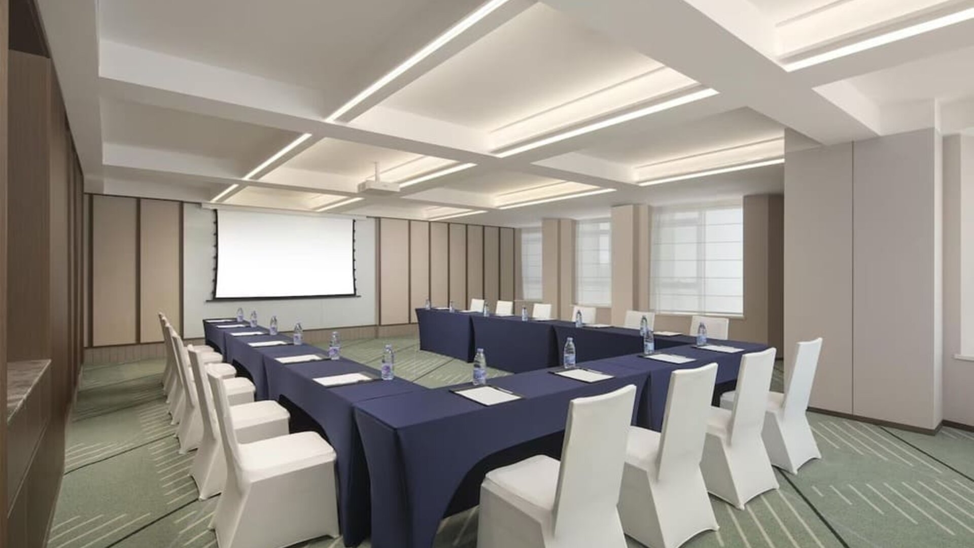 Conference room with U-shaped meeting setup, navy tablecloths, projector screen, and white chairs