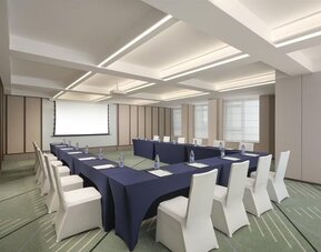 Conference room with U-shaped meeting setup, navy tablecloths, projector screen, and white chairs