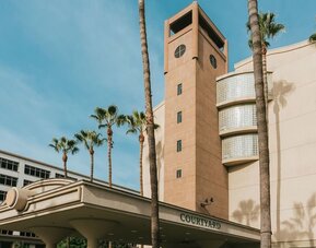 Daytime exterior entrance with tall palm trees and covered driveway at Courtyard By Marriott Los Angeles LAX/Century Boulevard.