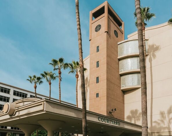Daytime exterior entrance with tall palm trees and covered driveway at Courtyard By Marriott Los Angeles LAX/Century Boulevard.