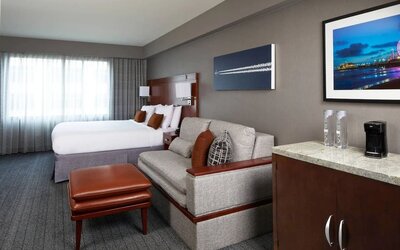 Spacious guest room with king bed, sofa seating area, ottoman, and kitchenette counter at Courtyard By Marriott Los Angeles LAX/Century Boulevard.
